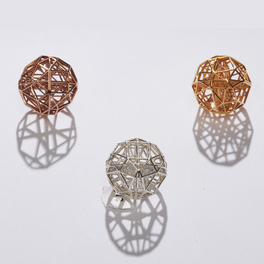 Three geometric sphere-shaped metal objects in rose gold, yellow gold, and silver casting shadows on a white surface