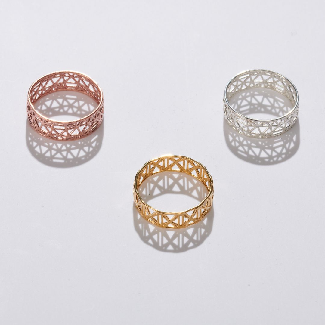 Three geometric metal rings in rose gold, yellow gold, and silver, casting shadows on a white surface.